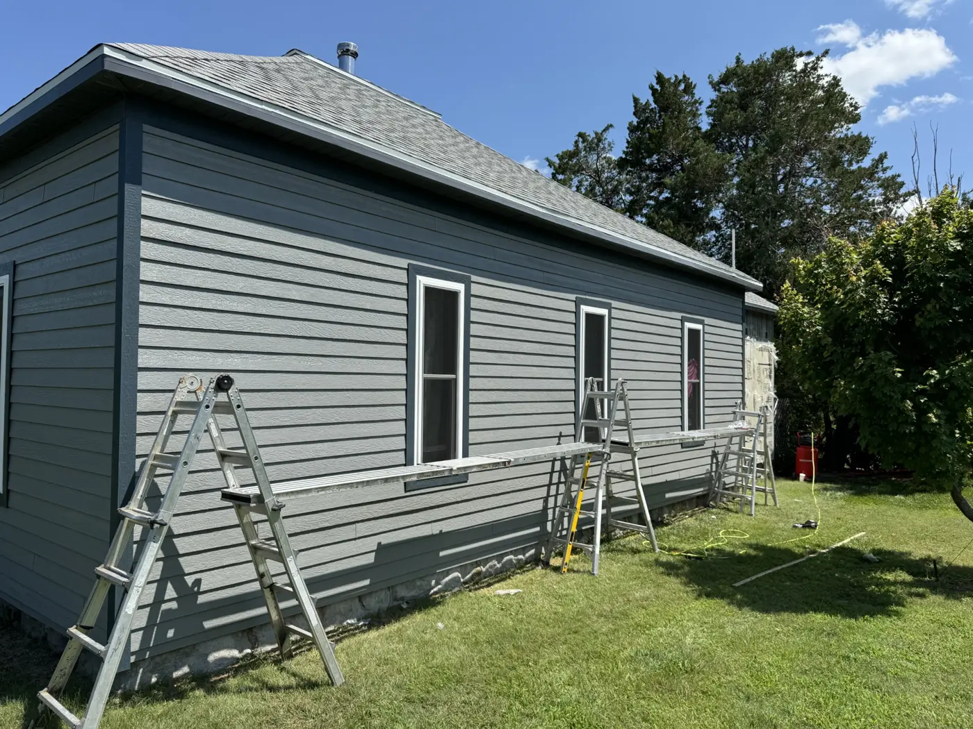 Siding and window trim installation progresses along the long side of the house.