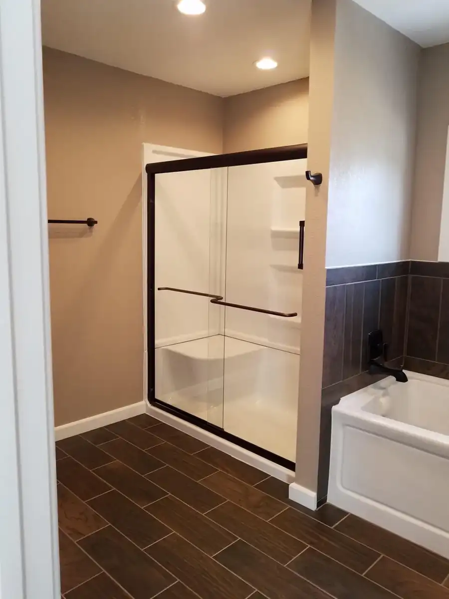 Finished glass shower enclosure beside bathtub and tiled floor