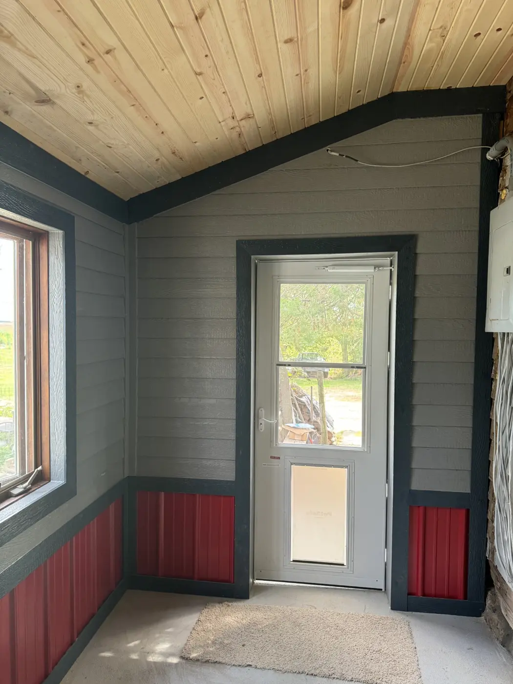 The porch interior features a wood ceiling, dark trim, and a contrasting lower wall finish around the entry.