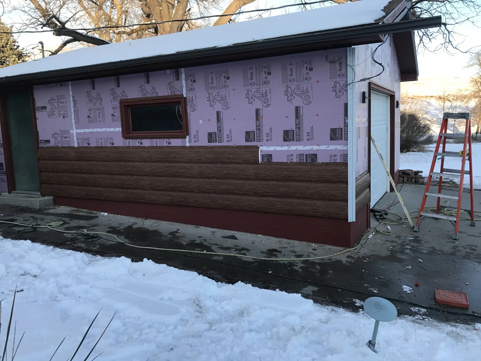 TruLog siding installed along the lower wall, with insulation board still exposed above as work progresses around the window.