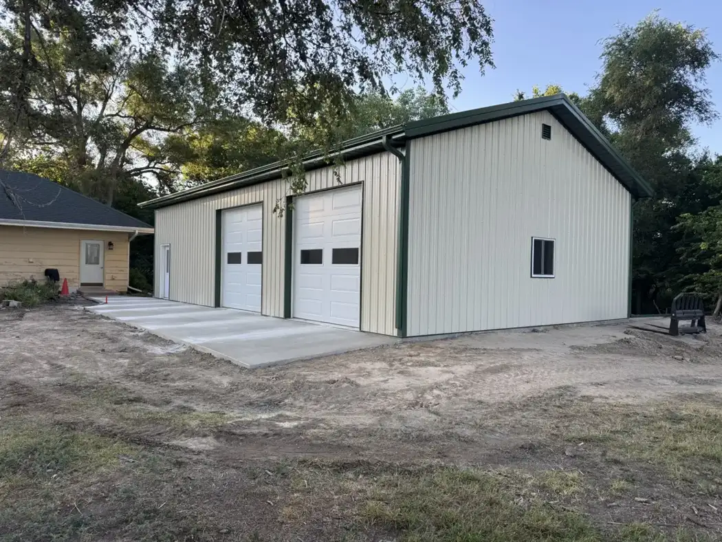 Metal siding, roof trim, two overhead doors, and a concrete apron complete the garage exterior.