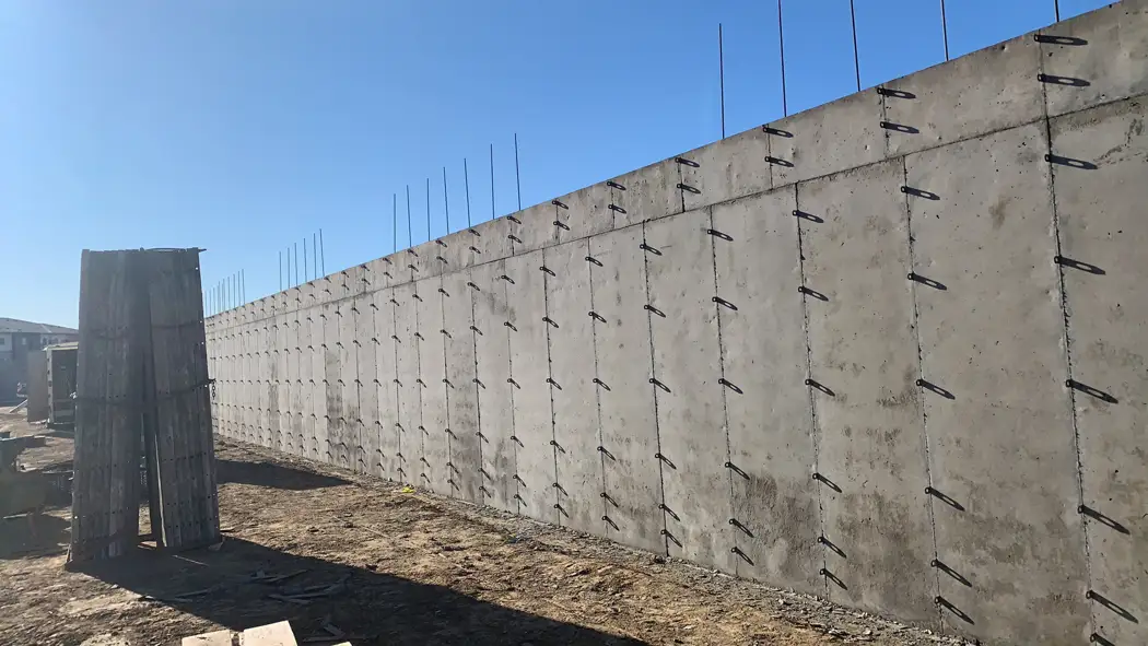 The poured concrete wall is exposed after form removal, with reinforcing bars extending above.