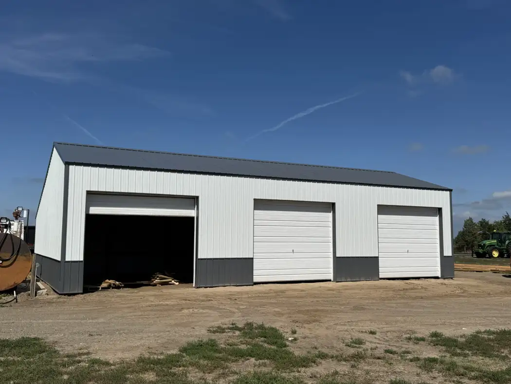 The finished front features three overhead-door bays, light metal siding, and a contrasting lower wall finish.
