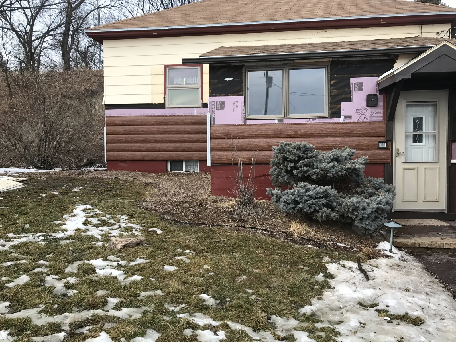 TruLog siding installation progresses across the house exterior, with the upper wall and window surround awaiting completion.