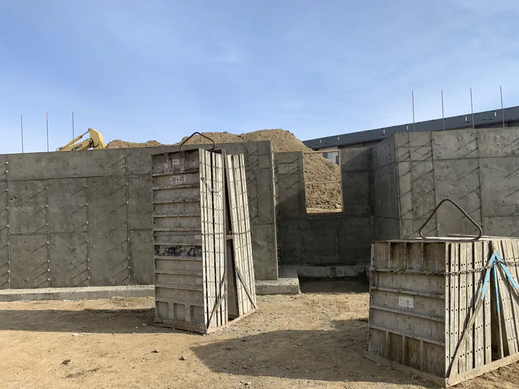 Completed wall sections and remaining form panels show the progress of the foundation work.
