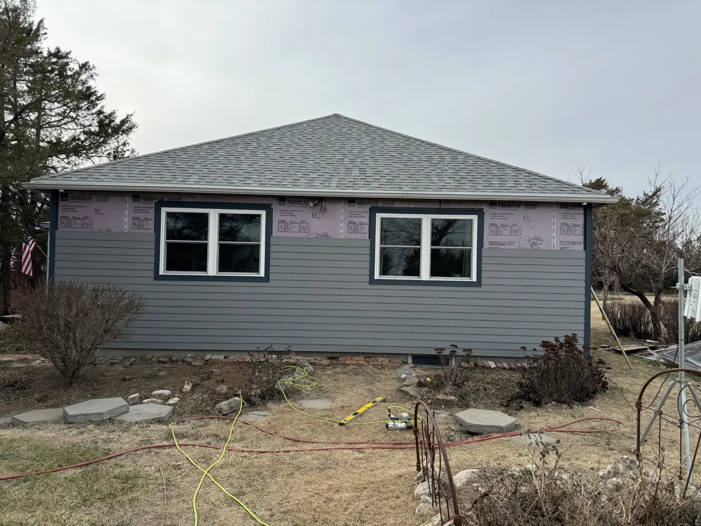 New siding progresses around the windows, with insulation board still visible along the upper wall.